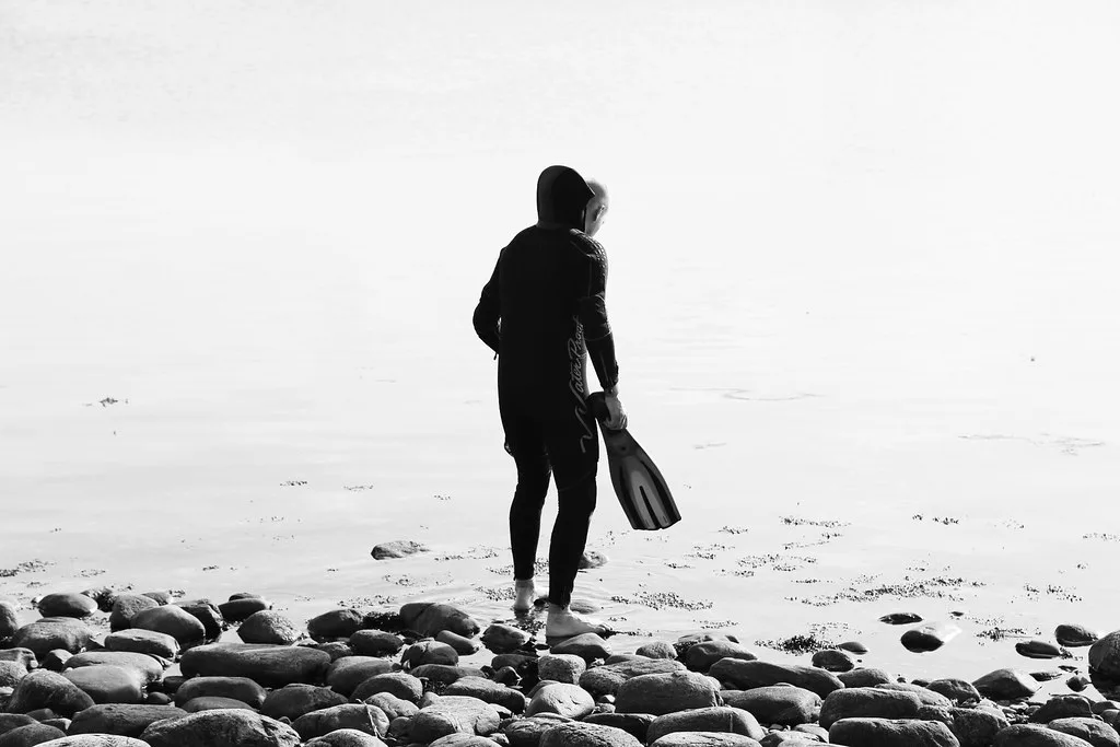 Snorkeler carrying fins across a cobble beach